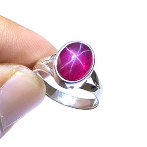 Könnte beinhalten: Ein silberner Ring mit einem roten Sternrubin-Edelstein. Der Rubin ist oval geformt und hat ein sternförmiges Muster.