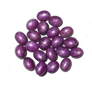 May include: A collection of 18 oval-shaped, purple star ruby gemstones. The stones have a star-like pattern in the centre.