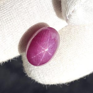 Könnte beinhalten: Ein rosafarbener Sternrubin-Cabochon mit einem sechszackigen Stern in der Mitte.