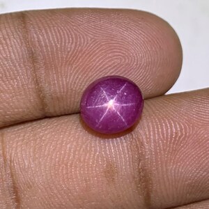 May include: A pink star ruby cabochon gemstone with a six-pointed star in the center.