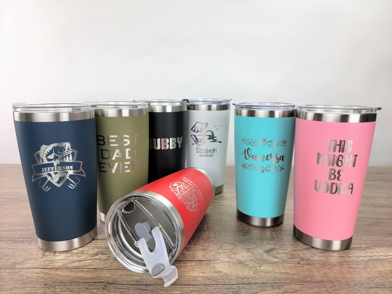 May include: Eight stainless steel tumblers with various colors and personalized engravings. The tumblers feature different designs and text, including "Best Dad Ever", "Hubby", "Elizabeth", "Vanessa", and "This Might Be Vodka".