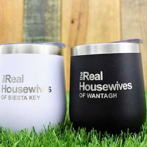 K&ouml;nnte beinhalten: Zwei Edelstahlbecher mit Deckeln. Der wei&szlig;e Becher hat den Text "the Real Housewives of Siesta Key" und der schwarze Becher hat den Text "the Real Housewives of Wantagh".