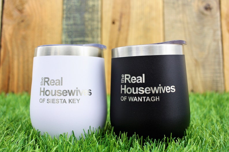 K&ouml;nnte beinhalten: Zwei Edelstahlbecher mit Deckeln. Der wei&szlig;e Becher hat den Text "the Real Housewives of Siesta Key" und der schwarze Becher hat den Text "the Real Housewives of Wantagh".
