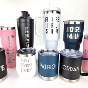 May include: A collection of nine personalized stainless steel tumblers and a shaker bottle. The tumblers are in various colors, including black, white, pink, and blue. The tumblers are engraved with names and phrases, such as "Nate", "Brittany", "Best Mom Ever", "Patrick", "Jordan", "Boss Man", "Future Is Now", and "Olivia".