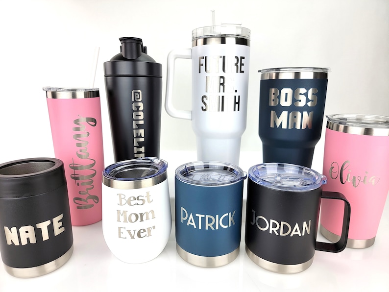 May include: A collection of nine personalized stainless steel tumblers and a shaker bottle. The tumblers are in various colors, including black, white, pink, and blue. The tumblers are engraved with names and phrases, such as "Nate", "Brittany", "Best Mom Ever", "Patrick", "Jordan", "Boss Man", "Future Is Now", and "Olivia".