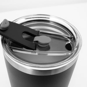 May include: A black stainless steel travel mug with a clear lid and a black plastic handle. The lid has a small gray button.