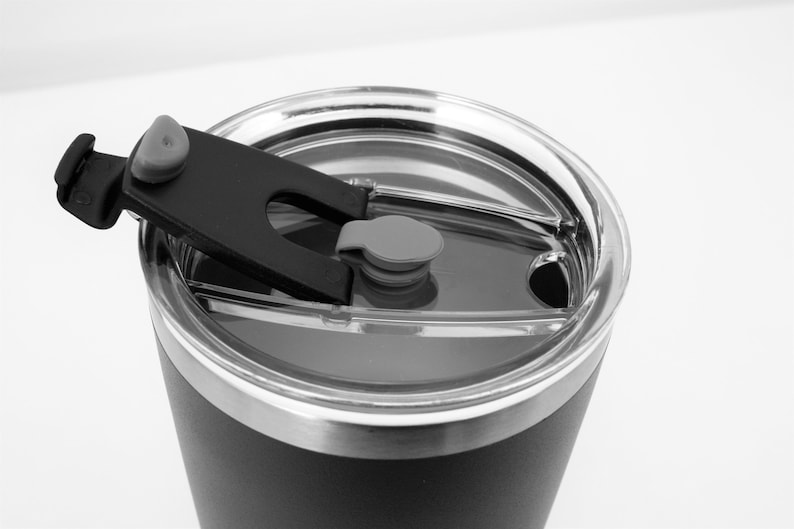 May include: A black stainless steel travel mug with a clear lid and a black plastic handle. The lid has a small gray button.