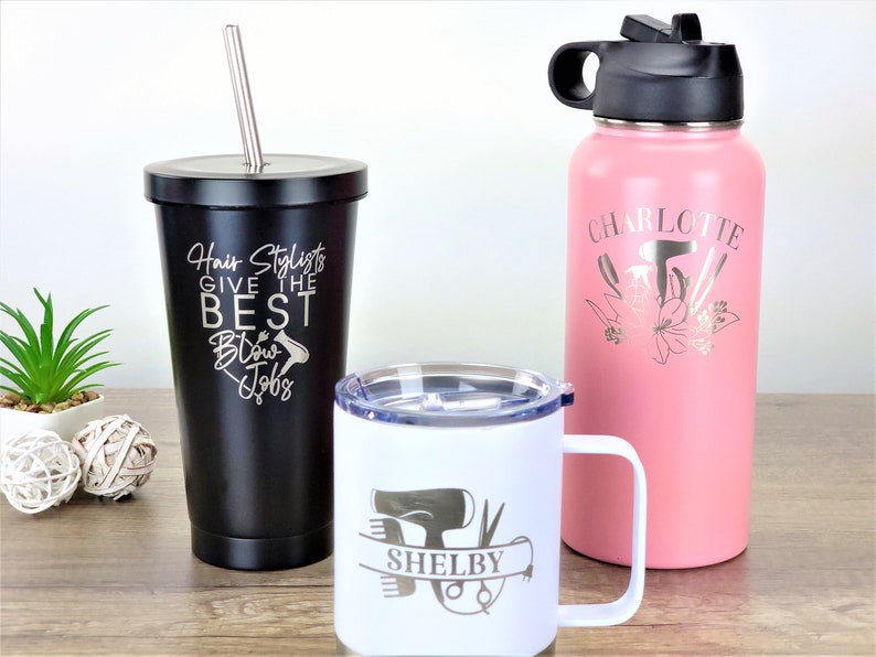 Puede incluir: Tres vasos de acero inoxidable con grabados personalizados. El vaso negro tiene el texto "Hair Stylists Give the Best Blow Jobs". El vaso blanco tiene un secador de pelo, tijeras y peines con el nombre "Shelby" grabado. El vaso rosa tiene un secador de pelo, tijeras y peines con el nombre "Charlotte" grabado.