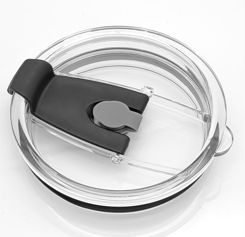 May include: A clear plastic lid with a black slider and a gray button. The lid is designed for a tumbler or cup.