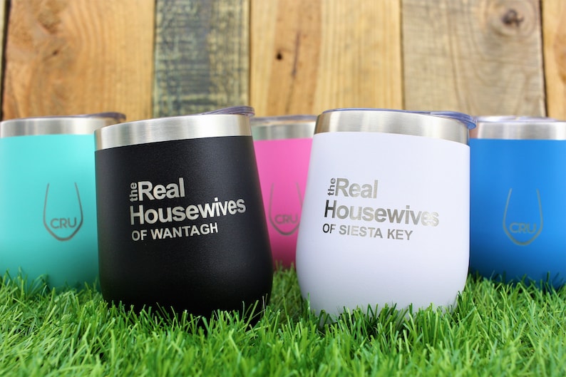 K&ouml;nnte beinhalten: F&uuml;nf Edelstahlbecher mit verschiedenen Farben f&uuml;r Deckel und K&ouml;rper. Die Becher tragen den Text "the Real Housewives" mit einem Ortsnamen darauf gedruckt. Die Becher stehen auf gr&uuml;nem Gras.