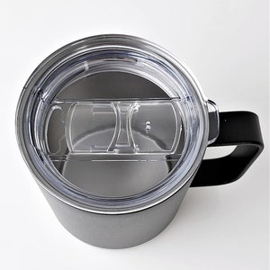 May include: A gray insulated travel mug with a black handle and a clear plastic lid. The lid has a sliding closure to open and close the drinking spout. The mug is designed to keep beverages hot or cold.