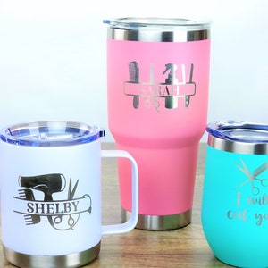 Puede incluir: Tres vasos de acero inoxidable con grabados personalizados para peluqueros. El vaso rosa dice "SARAH" con herramientas de peluquer&iacute;a. El vaso blanco dice "SHELBY" con un secador de pelo, tijeras y peines. El vaso turquesa dice "Te voy a cortar" con tijeras y una navaja.