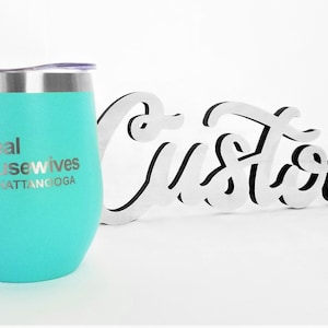 K&ouml;nnte beinhalten: Ein t&uuml;rkisfarbener Edelstahl-Weinglas mit dem Text "The Real Housewives of Chattanooga" eingraviert auf der Seite. Das Glas steht neben einem wei&szlig;en Holzschild mit der Aufschrift "Custom".