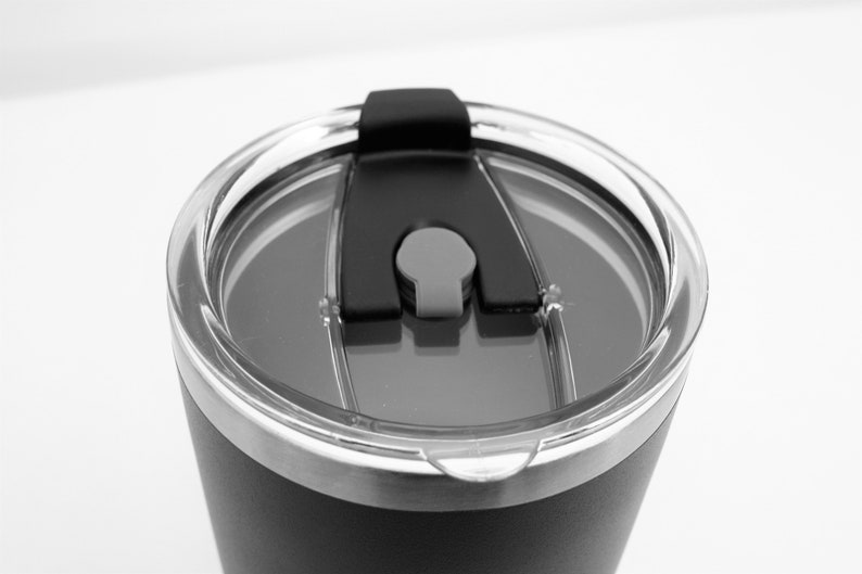 May include: Close-up of a black stainless steel travel mug with a clear lid and a black silicone slider.