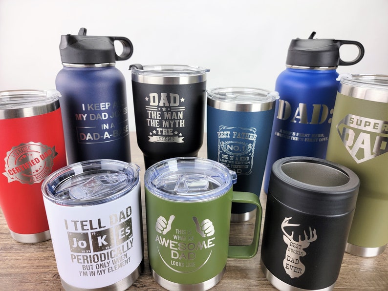 Puede incluir: Una colecci&oacute;n de vasos y tazas aislantes en varios colores, incluyendo rojo, negro, azul y verde. Cada vaso presenta texto grabado, con temas como "Pap&aacute;", "Mejor Padre" y frases humor&iacute;sticas. Los vasos tienen una capacidad de aproximadamente 570-850 ml.