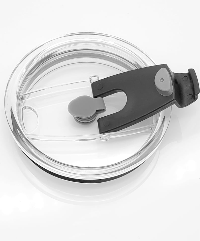 May include: A clear plastic lid with a black slider and a gray button. The lid is designed for a travel mug or tumbler.