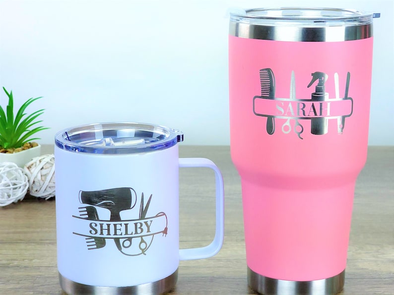 Puede incluir: Dos tazas de viaje de acero inoxidable con nombres personalizados y herramientas de peluquer&iacute;a. La taza m&aacute;s grande es rosa y dice "SARAH" y la taza m&aacute;s peque&ntilde;a es blanca y dice "SHELBY".