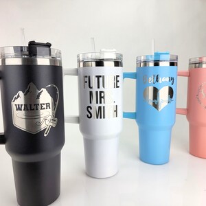 May include: Four stainless steel travel mugs with personalized engravings. The mugs are black, white, light blue, and pink. The engravings include "Walter" with a mountain and fishing rod design, "Future Mrs. Smith", "Bethany" with a heart and EKG line, and "Sarah Bride" with a wreath.