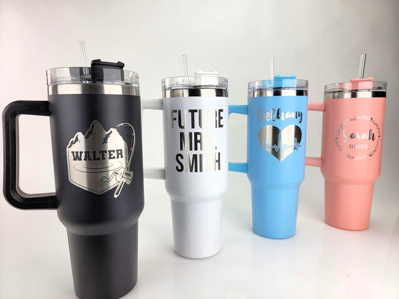 May include: Four stainless steel travel mugs with personalized engravings. The mugs are black, white, light blue, and pink. The engravings include "Walter" with a mountain and fishing rod design, "Future Mrs. Smith", "Bethany" with a heart and EKG line, and "Sarah Bride" with a wreath.