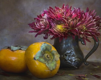 May include: A still life featuring two ripe persimmons and a bouquet of deep pink and burgundy dahlias in a pewter pitcher.