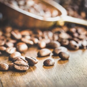 May include: Close-up of roasted coffee beans scattered on a wooden surface. The beans are brown and have a rich, earthy aroma.