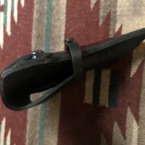 Puede incluir: Una funda de cuero negra con un mango de madera marr&oacute;n. La funda tiene una correa y un cierre de presi&oacute;n met&aacute;lico.