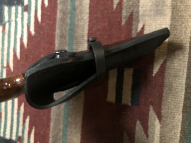Puede incluir: Una funda de cuero negra con un mango de madera marr&oacute;n. La funda tiene una correa y un cierre de presi&oacute;n met&aacute;lico.