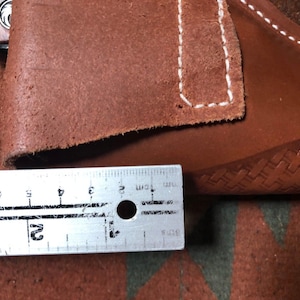 Op de afbeelding: Een bruine leren holster met witte stiksels. De holster wordt gemeten met een liniaal, wat een lengte van 7,6 cm laat zien.