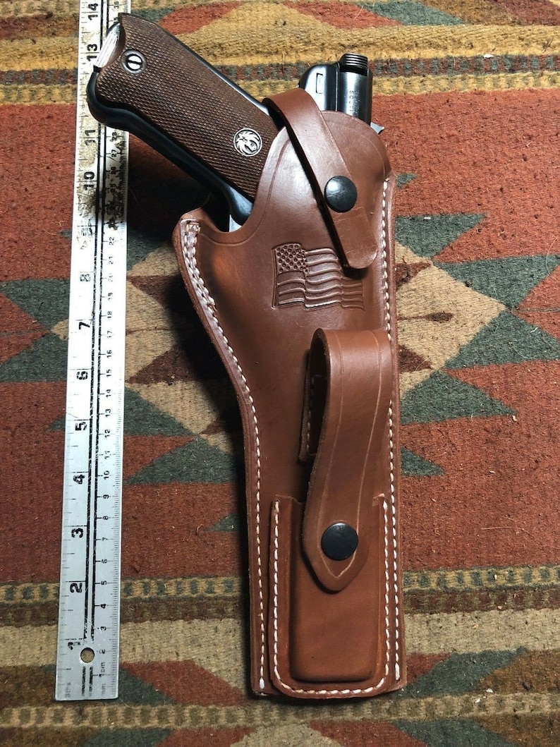 Puede incluir: Una funda de cuero marr&oacute;n con detalles de costura blanca. La funda tiene una solapa con un bot&oacute;n negro y un peque&ntilde;o bolsillo con un bot&oacute;n negro. La funda est&aacute; dise&ntilde;ada para sostener un arma de fuego. Una bandera estadounidense est&aacute; grabada en la funda.