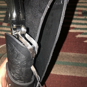Peut inclure: Un &eacute;tui en cuir noir avec une boucle argent&eacute;e et un pistolet noir &agrave; l'int&eacute;rieur. L'&eacute;tui a un motif d&eacute;coratif sur le devant.