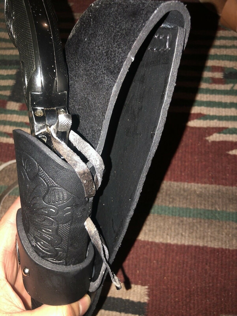 Peut inclure: Un &eacute;tui en cuir noir avec une boucle argent&eacute;e et un pistolet noir &agrave; l'int&eacute;rieur. L'&eacute;tui a un motif d&eacute;coratif sur le devant.