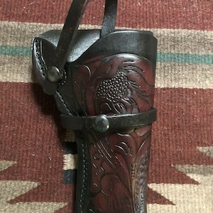 Puede incluir: Una funda de cuero marr&oacute;n con un dise&ntilde;o floral y una correa. La funda tiene un bot&oacute;n de metal y un lazo para llevar.