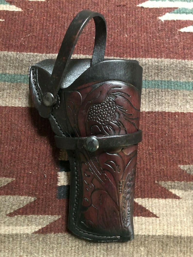 Puede incluir: Una funda de cuero marr&oacute;n con un dise&ntilde;o floral y una correa. La funda tiene un bot&oacute;n de metal y un lazo para llevar.