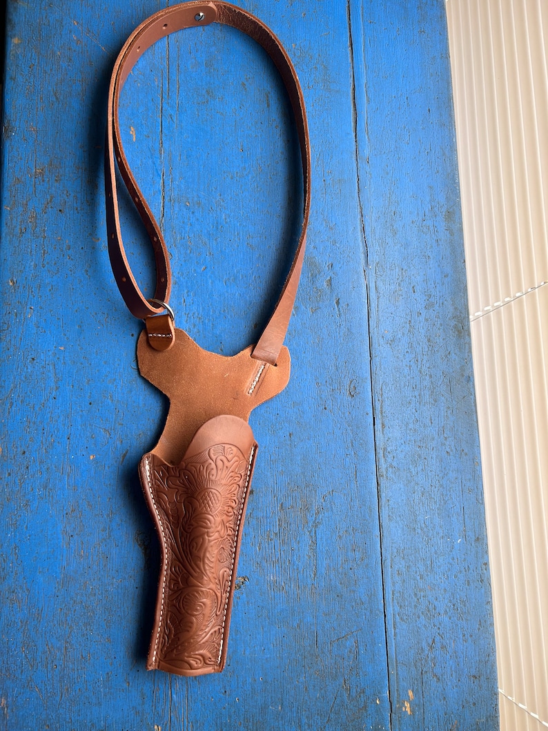 Puede incluir: Una funda de cuero marr&oacute;n con un dise&ntilde;o floral. La funda est&aacute; unida a una correa de cuero marr&oacute;n que se puede llevar sobre el hombro.