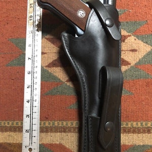 May include: A black leather holster for a handgun with a brown grip. The holster has a belt loop and a snap closure.