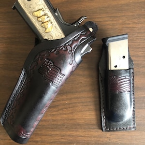 Puede incluir: Una funda de cuero marr&oacute;n con un dise&ntilde;o de bandera estadounidense, que contiene una pistola grabada en plata y oro. Una funda de cuero marr&oacute;n separada con un dise&ntilde;o de bandera estadounidense contiene un cargador plateado.