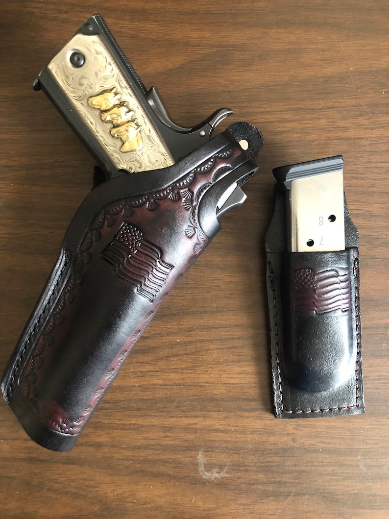 Puede incluir: Una funda de cuero marr&oacute;n con un dise&ntilde;o de bandera estadounidense, que contiene una pistola grabada en plata y oro. Una funda de cuero marr&oacute;n separada con un dise&ntilde;o de bandera estadounidense contiene un cargador plateado.