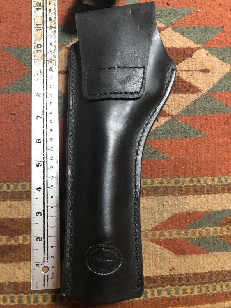 May include: A black leather holster with a stitched design and a circular embossed logo that reads "Tom's Custom Leather".
