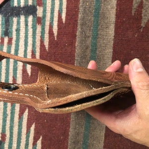 May include: A brown leather holster with stitching detail. The holster is open and folded in half, showing the inside lining.