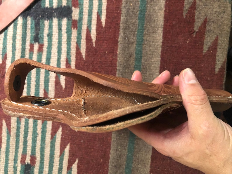 May include: A brown leather holster with stitching detail. The holster is open and folded in half, showing the inside lining.