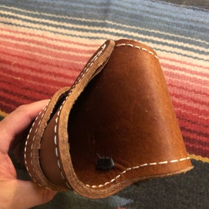 May include: A brown leather holster with white stitching. The holster is folded in half and the inside is visible.