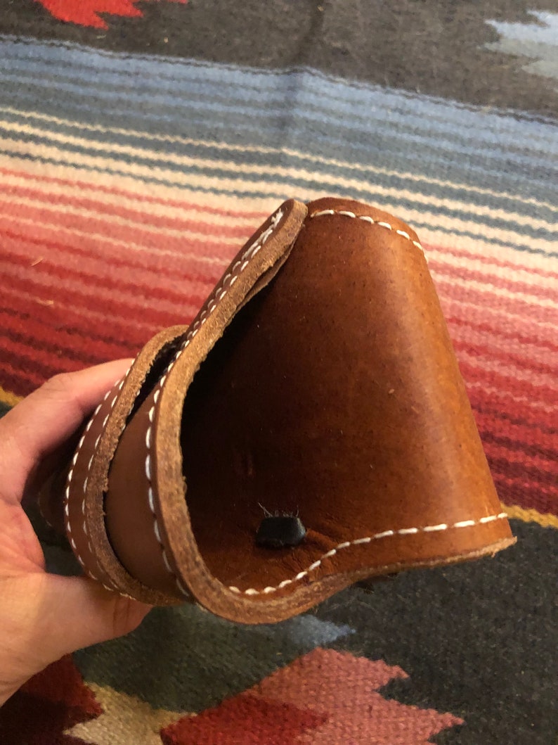 May include: A brown leather holster with white stitching. The holster is folded in half and the inside is visible.