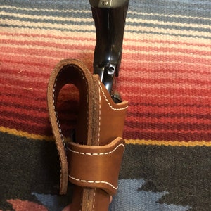 May include: A brown leather holster with white stitching for a black handgun.