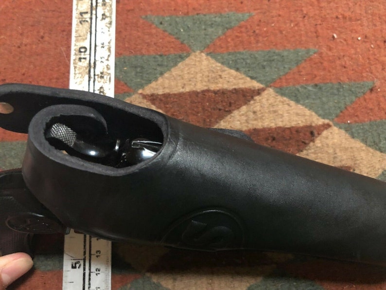Pode incluir: Um coldre de couro preto para uma pistola. O coldre &eacute; projetado para se ajustar perfeitamente &agrave; arma e tem uma aba que cobre o gatilho.