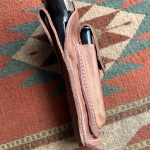 May include: A brown leather holster with a stitched edge and a silver-toned gun inside.