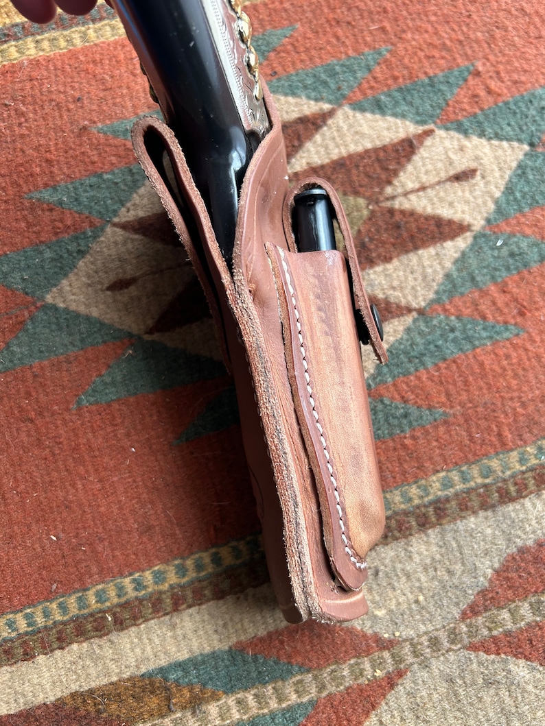May include: A brown leather holster with a stitched edge and a silver-toned gun inside.