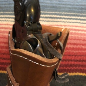 May include: A brown leather holster with white stitching and a black strap. A black revolver is inside the holster.