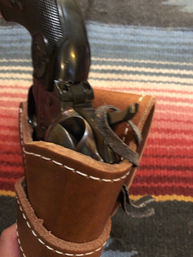 May include: A brown leather holster with white stitching and a black strap. A black revolver is inside the holster.