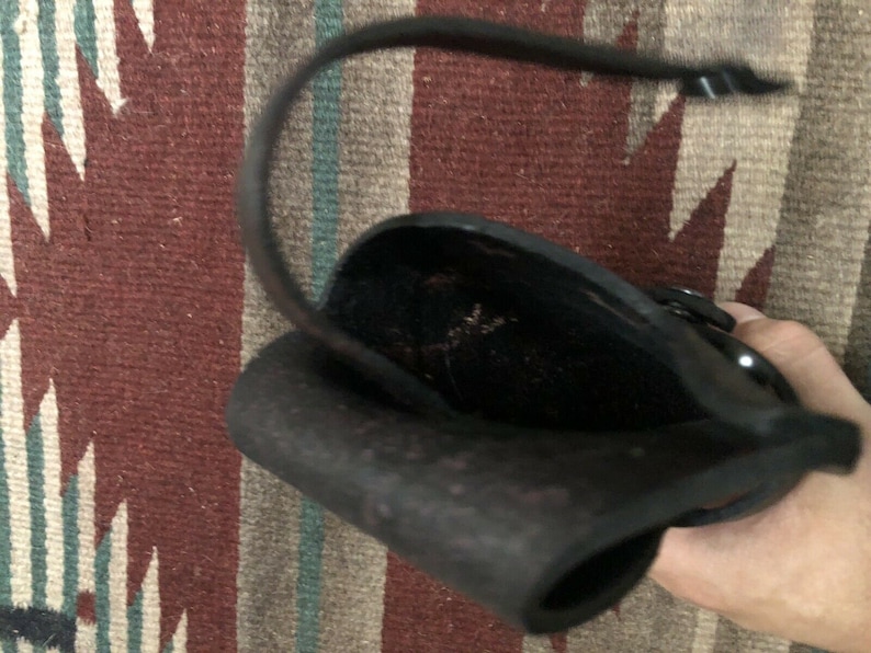 Puede incluir: Una funda de cuero negra con una solapa que se cierra con un broche a presi&oacute;n. La funda est&aacute; dise&ntilde;ada para sostener un objeto peque&ntilde;o, como un cuchillo o una herramienta.