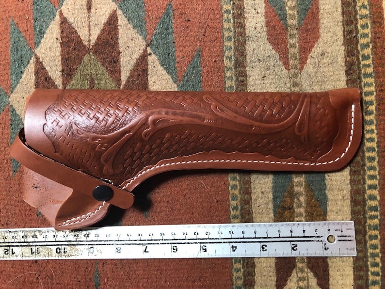Op de afbeelding: Een bruine leren holster met een geweven patroon en witte stiksels. De holster is 23 cm lang.